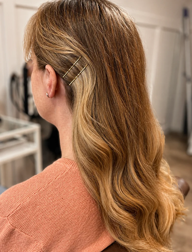 Blond balayage med mjuka vågor och guldiga hårspännen, stylat hos Hair by Isabelle i Aneby.